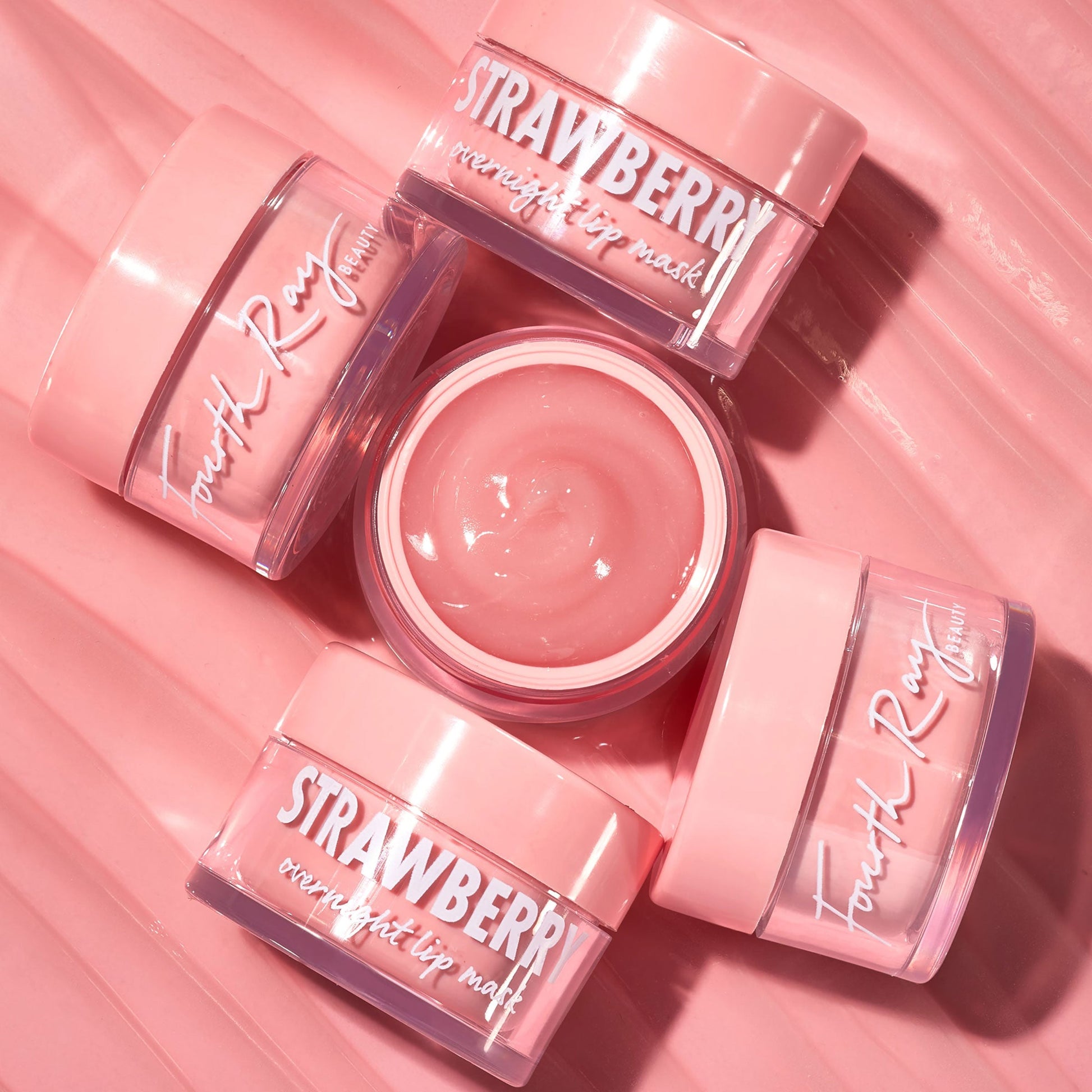Strawberry lip mask jars displaying an open pot of glossy pink balm, arranged on a rippled pink backdrop; ColourPop Fourth Ray Beauty overnight lip mask in pastel pink acrylic pots with white script logos.