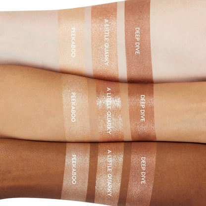 ColourPop A Little Quarky Super Shock Shadow swatched on light, medium, and deep skin, shown between Peekaboo and Deep Dive; warm champagne metallic shimmer with high shine and creamy texture, displayed in trio arm swatches for shade comparison.
