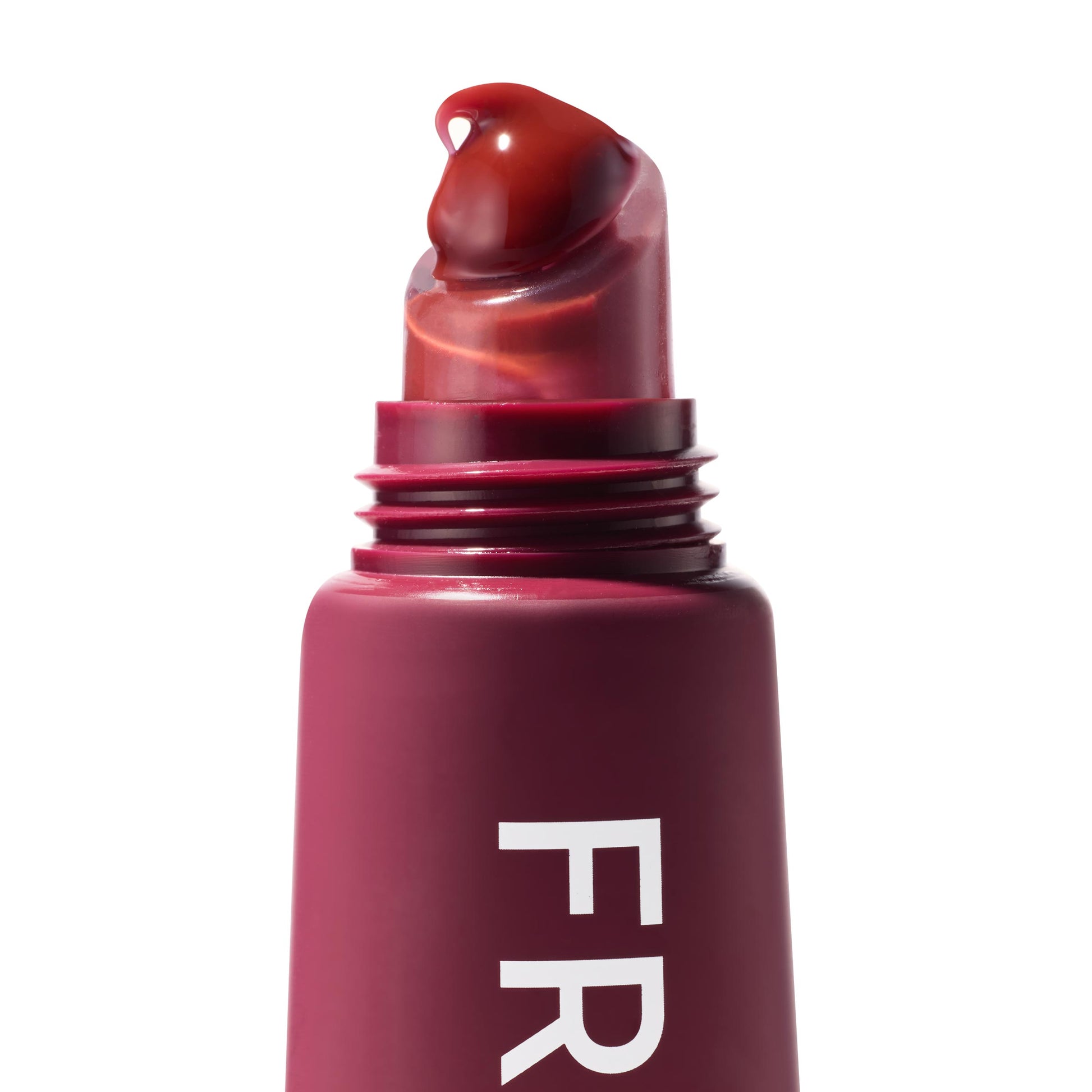 Wild Berry ColourPop Fresh Kiss Glossy Balm applicator releasing a droplet of rich berry gloss from a slanted clear tip, shown in a macro close-up with the maroon tube and partial FR lettering against a white background.