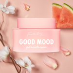 Good Mood Gel Moisturizer jar by Fourth Ray Beauty sits centered on a blush-pink backdrop, the pink frosted container with white lettering surrounded by white blossoms, petals, and watermelon slices - styled ColourPop Face Moisturizer product shot.