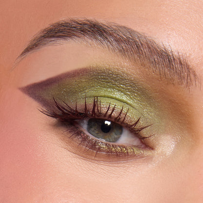 Close-up eye wearing the ColourPop Beware Ogre shadow palette, with shimmering lime and olive greens blended into a deep plum cut-crease wing, soft inner-corner glow, and defined lashes, shown on skin to highlight pigment and finish.