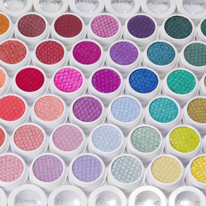 ColourPop Super Shock Shadow Frog single glistening in an open white pot, displayed in a flat‑lay rainbow grid of other Super Shock Shadow pots with scale-textured surfaces and ColourPop lids.